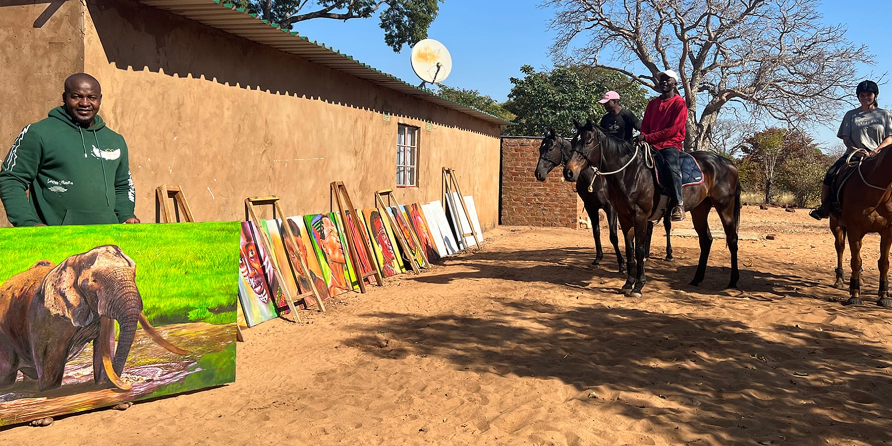 Local Zimbabwean artist displaying colorful paintings and crafts for riders at Wild Bhiza village tour in Chisuma Village near Victoria Falls supporting community artists