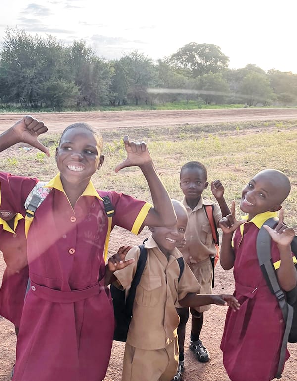 Local-School-Children-Village-Life-Wild-Bhiza-Community-Chisuma-Zimbabwe Happy local schoolchildren in uniforms waving and smiling in Chisuma Village Zimbabwe where Wild Bhiza operates community programs near Victoria Falls