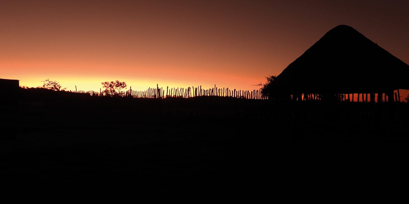 Traditional African rondavel silhouetted against a golden sunset near Victoria Falls, Zimbabwe showcasing an authentic homestead accommodation experience